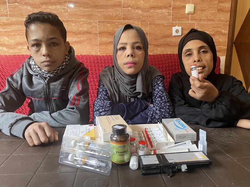 Three people sit at a table laden with medicines