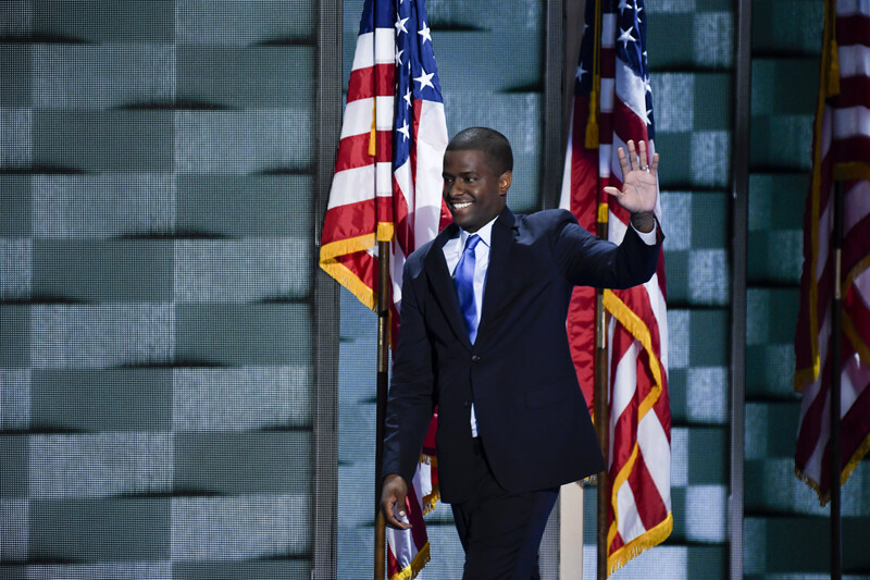 Man waves with American flags behind him