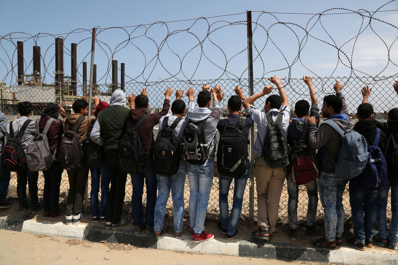 Palestinian students look through barbed wire at power plant
