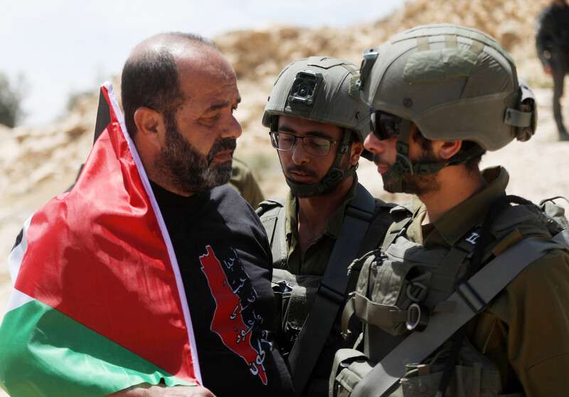 A man with a Palestinian flag confronts two soldiers