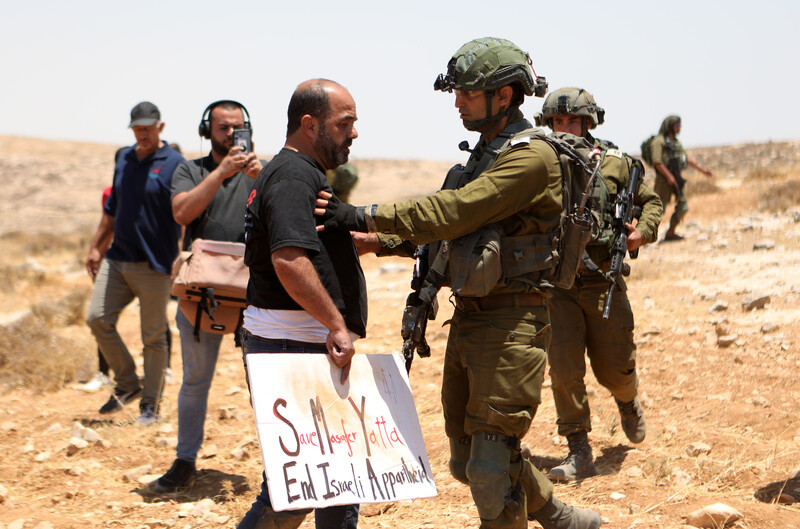 A man holding a sign is pushed by an Israeli soldier