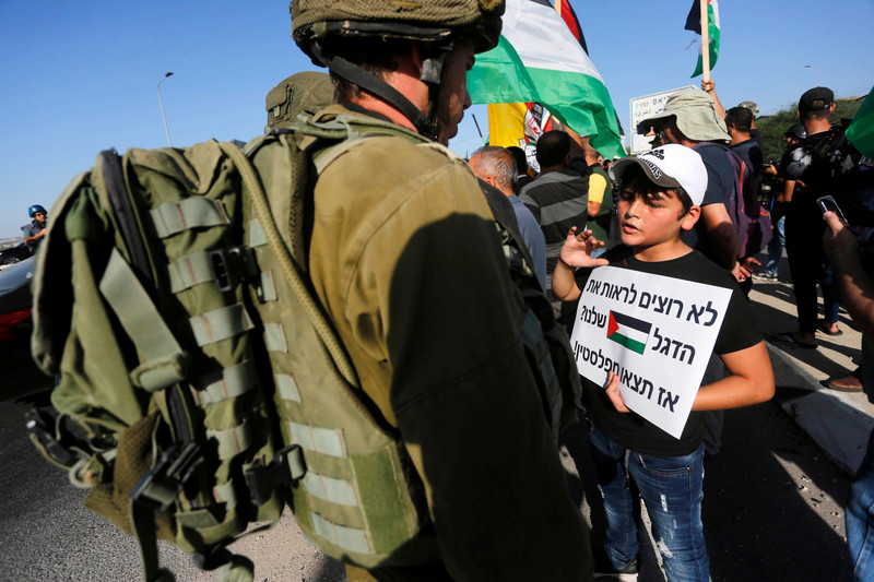 Palestinians confront Israeli forces after an attempt by Israeli settlers to remove Palestinian flag in Izbet al-Tabib village east of the central West Bank city of Qalqilya, on 9 June. The boy’s sign reads “Don’t want to see the Palestinian flag? Then get out of Palestine!” in Hebrew.  (Shadi Jarar’ah/ APA images)
