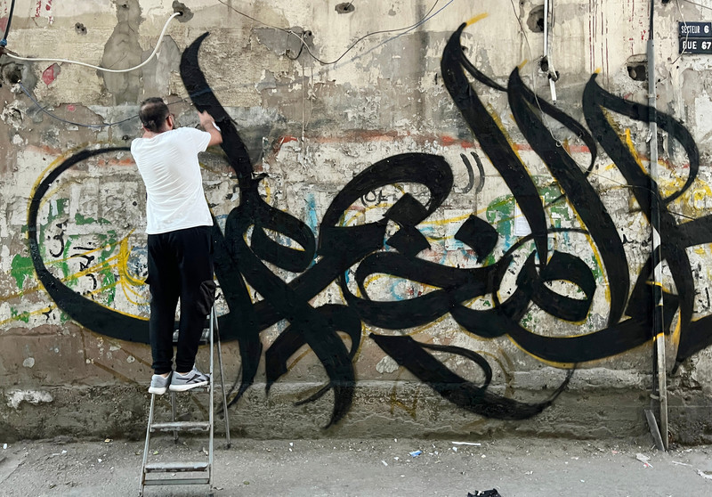 Palestinian artist Bilal Khaled paints calligraphy reading “in the name of the camp, I did not die, ask Jenin” in Burj al-Barajneh, a Palestinian refugee camp in the Lebanese capital Beirut on 10 June. (Nidal Al-Wahidi/ APA images)