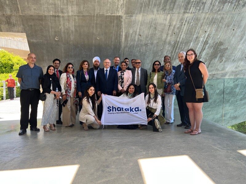 Group of people pose with a banner that says "Sharaka" 