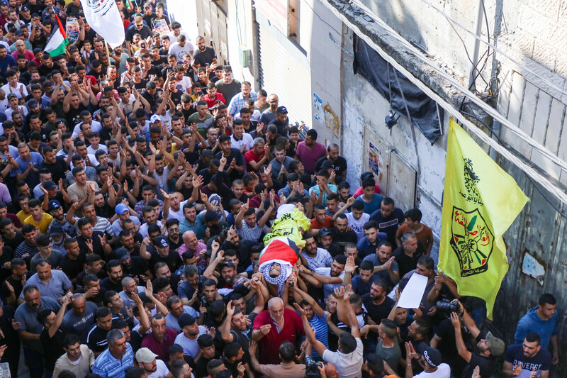 Dozens of people carry the body of a boy. wrapped in a flag on a stretcher 