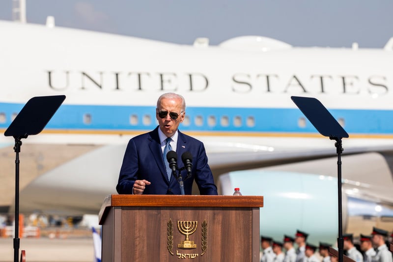Joe Biden in sunglasses stands at a speaker's podium before Airforce 1