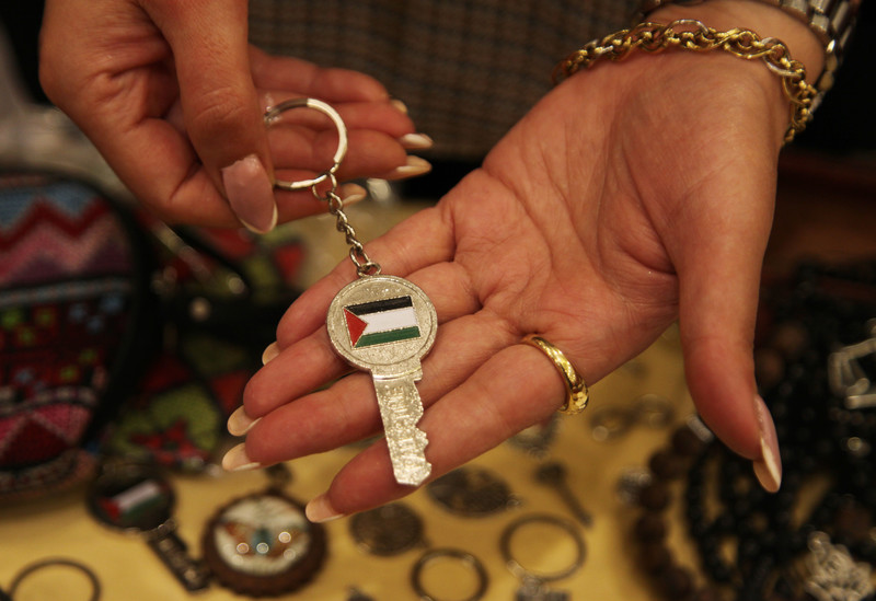A woman holds a key bearing the Palestinian flag in her hand