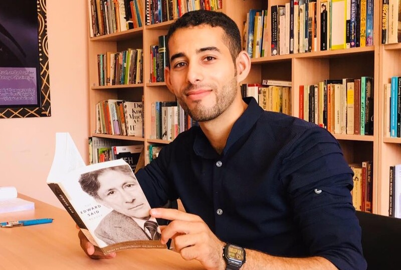 Mosab Abu Toha sits at a table in the Edward Said Library holding a book