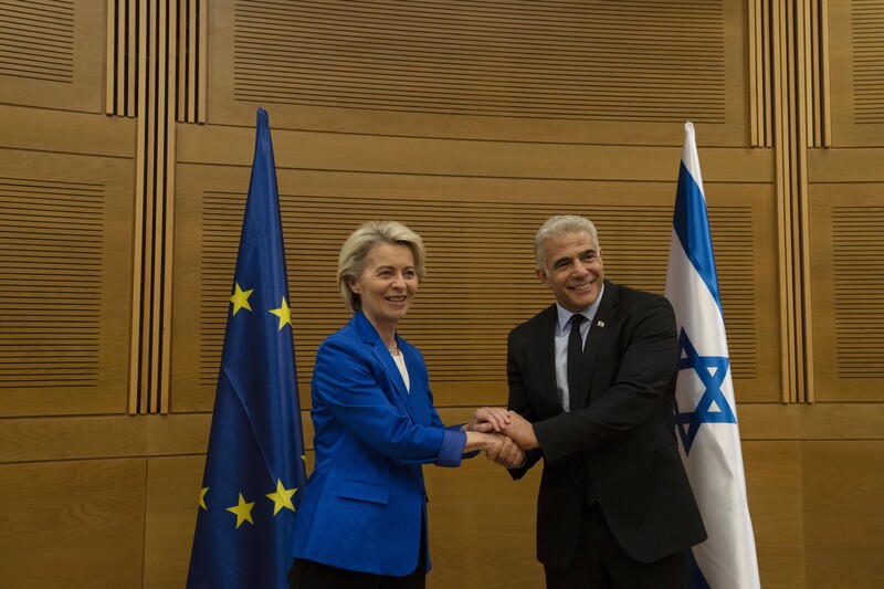 Man and woman clasp hands in front of EU and Israeli flags