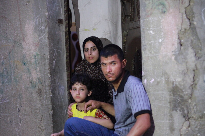 Joud al-Amarin, age 6, who was diagnosed with leukemia, stands hear her mother and father.