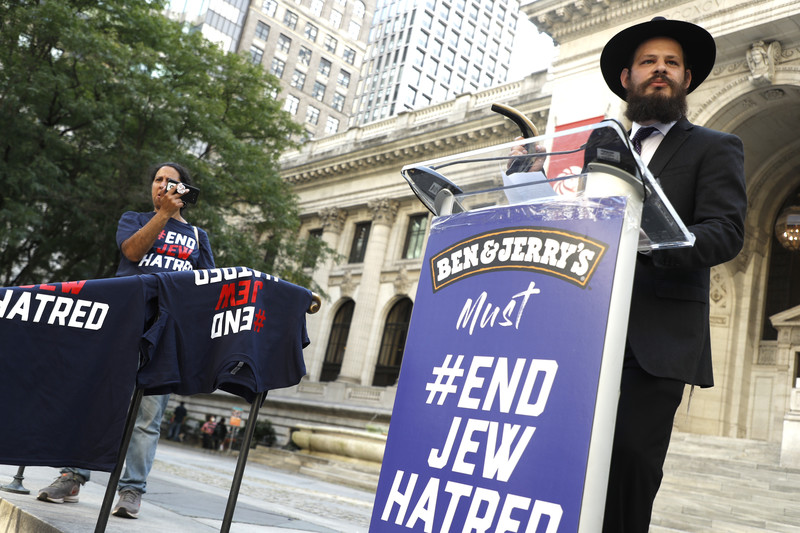 Man stands at podium that says on it Ben and Jerry's must end Jew hatred
