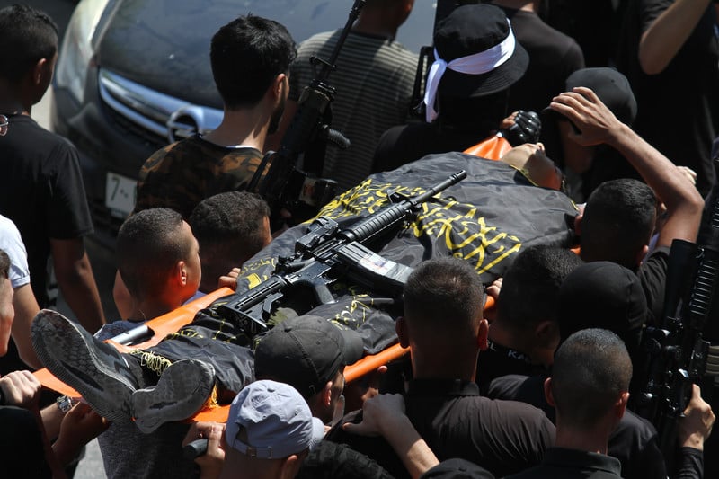 Men carry a flag-wrapped body on a stretcher with a weapon on top 