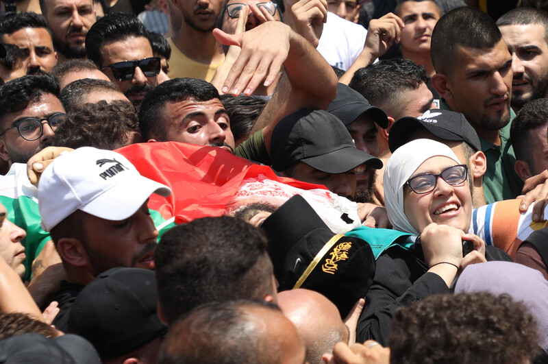 A woman among a group of man carrying a flag-draped stretcher