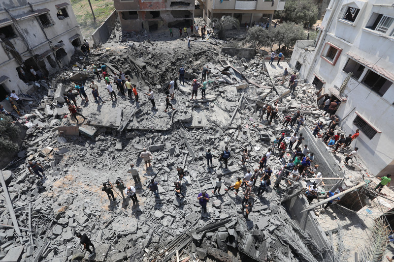 People stand atop the ruins of a destroyed building 