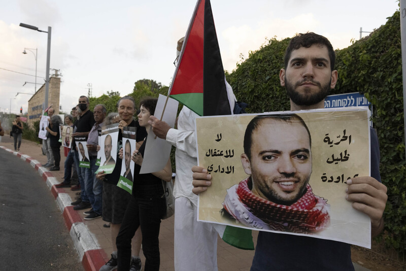 People hold posters and flags on the sidewalk 