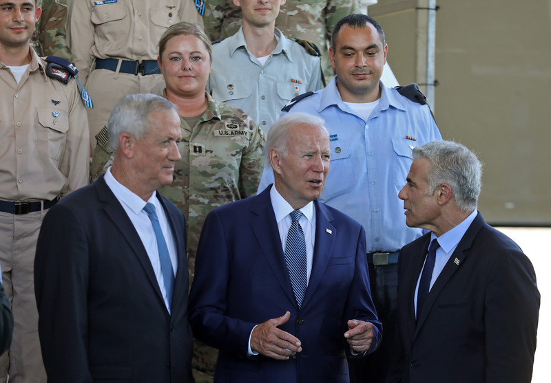 Three men in suits stand in front of military personnel