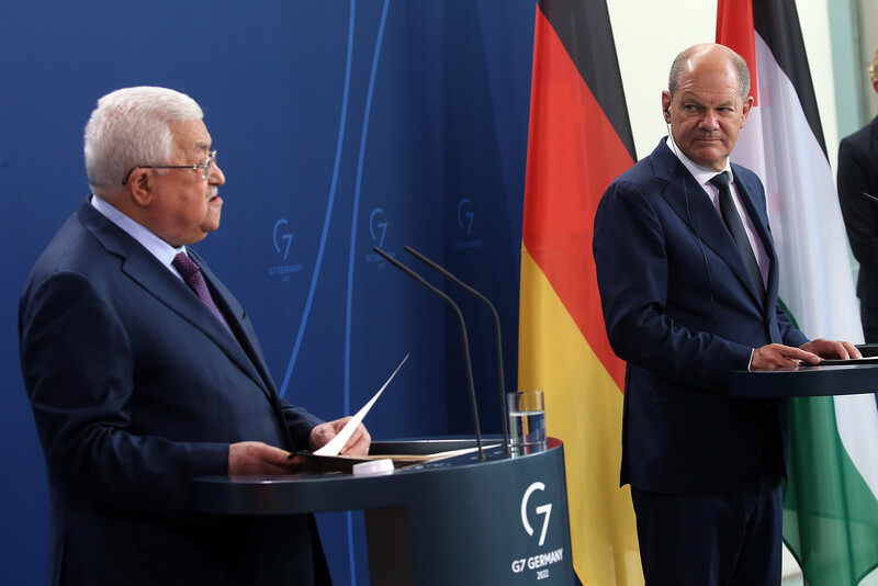 Two men stand at podiums with German and Palestinian flags