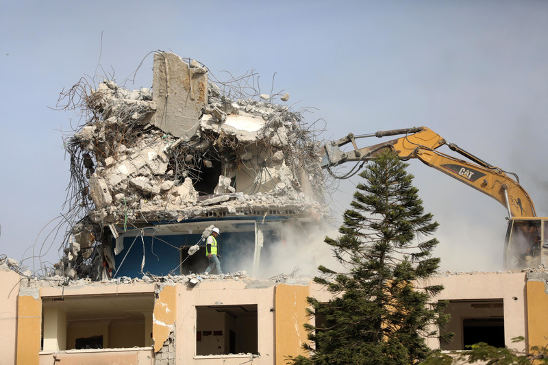 Dust rises as bulldozers work on a bombed out building