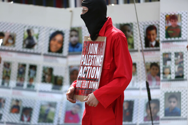 A masked man with a poster stands in front of pictures of children slain in Gaza