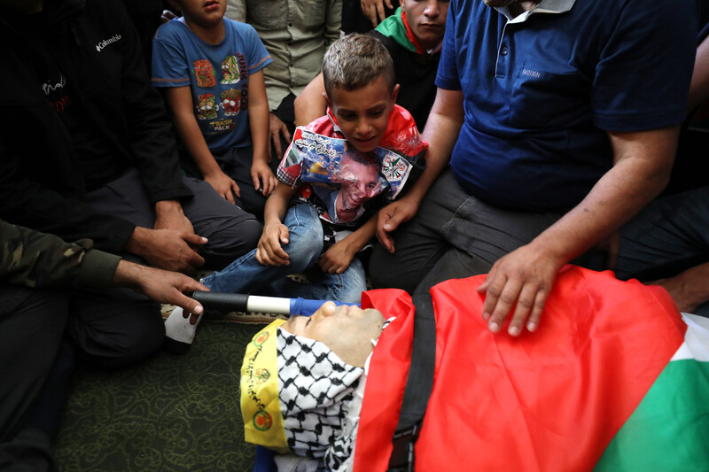 Boy looks over man's body while surrounding by people 