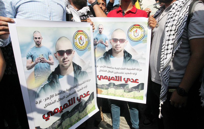 People hold two identical posters side by side showing the face of a bald man wearing sunglasses 