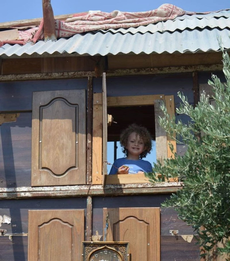 A child looks out the window of a small dwelling