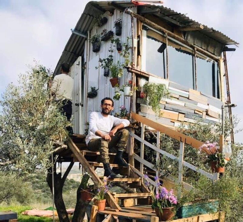 A man sits on steps leading up to a small dwelling