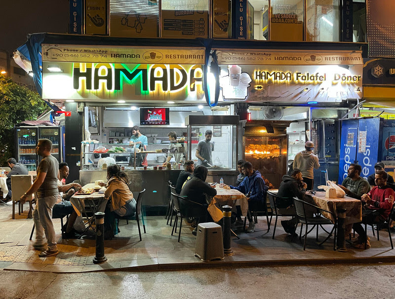 People sit at tables on sidewalk in front of diner at night