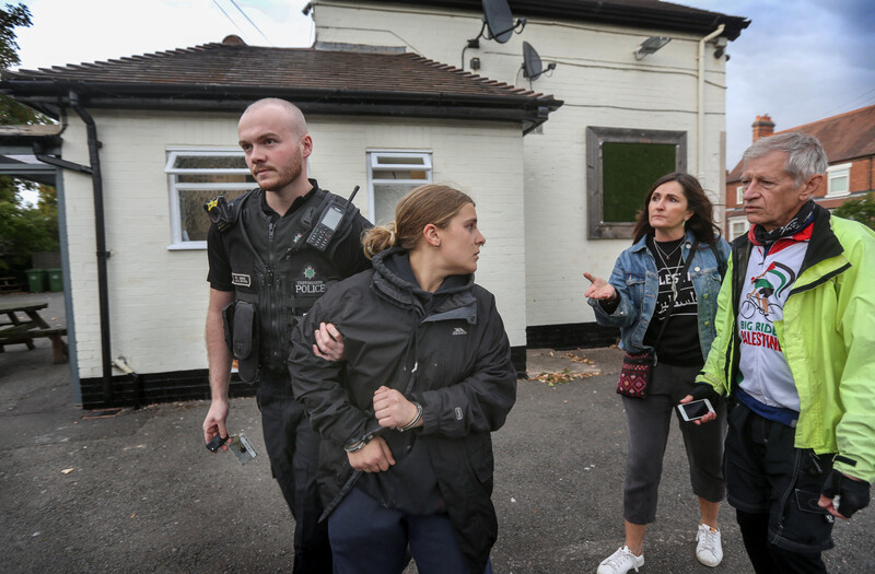 A police officer takes away a handcuffed woman, turning to speak to two others behind her