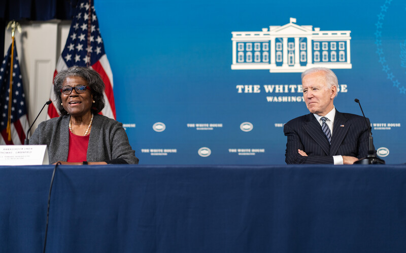 Two people sit at a table with American flags behind them