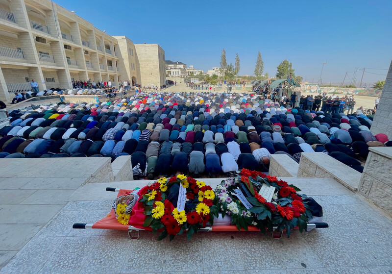 People pray before someone's corpse on a stretcher adorned with flowers 