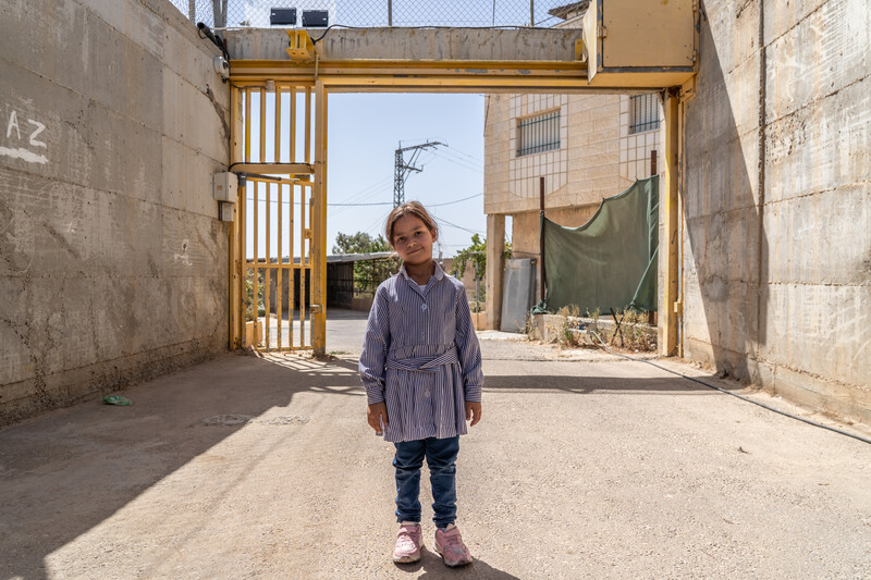 A girl stands before a yellow metal gate