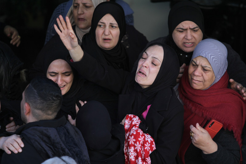 A group of women dressed in headscarves mourning, with one woman stretching her arms out