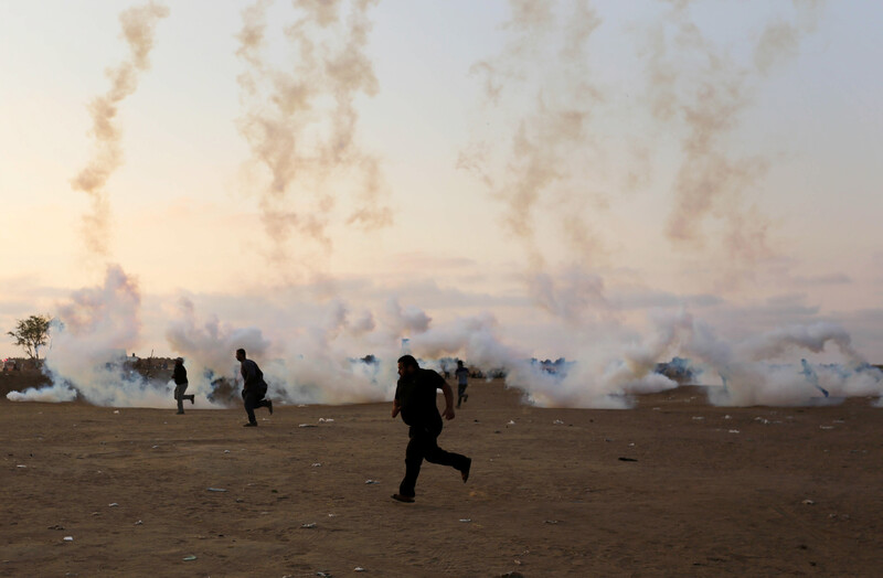 Clouds of tear gas smoke rise from canisters on the ground as a group of Palestinian men run for safety