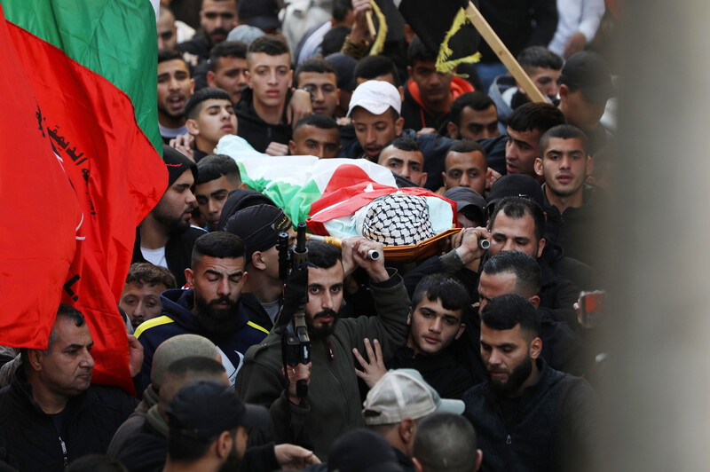 Men carry the coffin of a boy wrapped in a flag, some of them carrying rifles