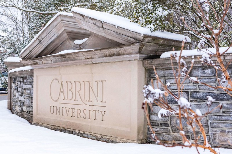 Snow and bushes surround a stone sign with the name of the university