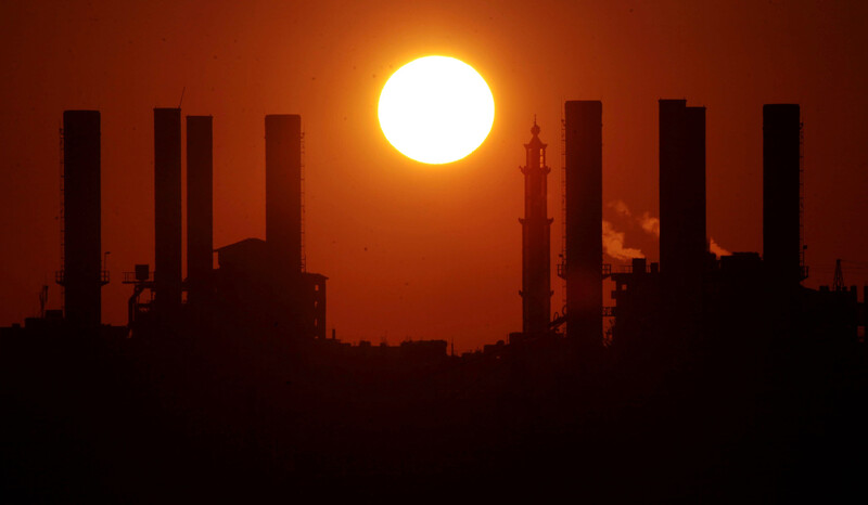 A giant yellow sun sets over the silhouette of a Gaza power station