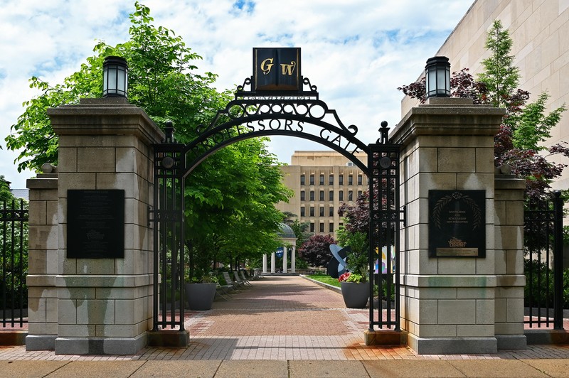 A gate in the campus of George Washington University arcs between two concrete pillars.