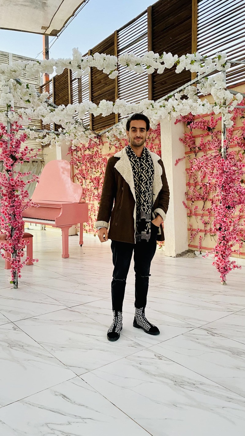 A man stands in front of a colorful flower arrangement and a pink piano
