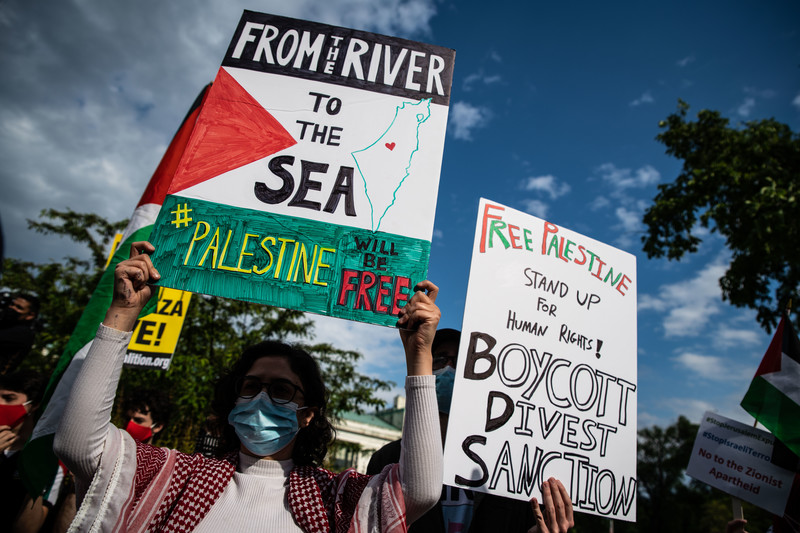 Protesters hold signs above their heads, one calling for boycott, divestment and sanctions against Israel and the other calling for Palestine to be free from the river to the sea.