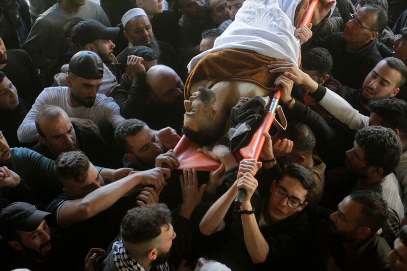 A group of men are seen carrying a stretcher with the body of a man covered in a white sheet