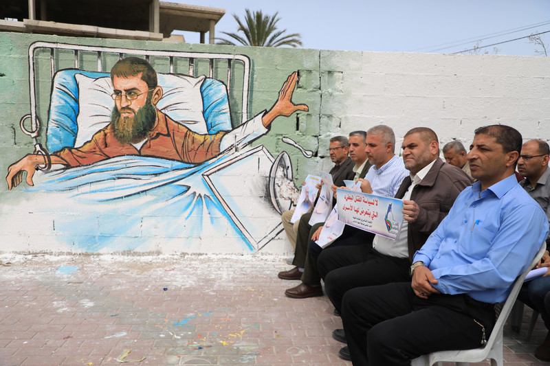 Men are seated near a mural that depicts a prisoner in a hospital bed 