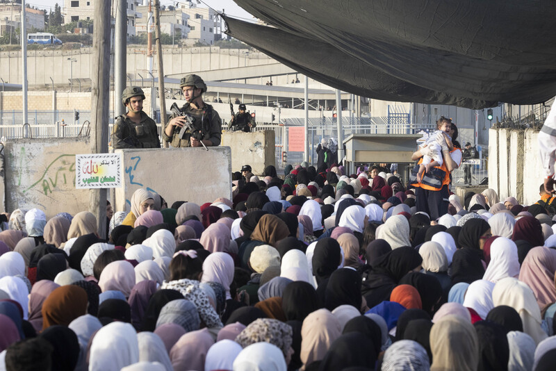 Two Israeli soldiers at a checkpoint watch as hundreds of Palestinians line up in order to pass through.