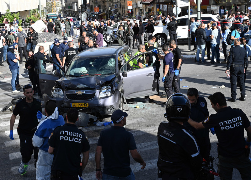 A battered SUV in a crosswalk is surrounded by police, first responders and onlookers
