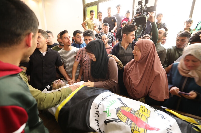 Crying woman stand over the body of a young man shrouded in Islamic Jihad flag in crowded room