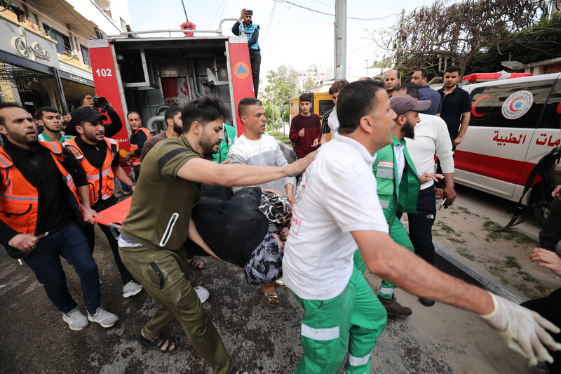 Men, some wearing paramedics clothing, carry a person on a stretcher near a fire truck and ambulance