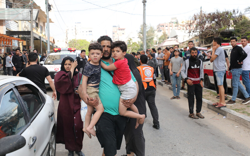 A man holds two young boys in his arms as people gather in street