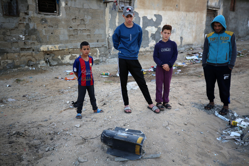 Four children stand near and observe an exploded missile on the ground 