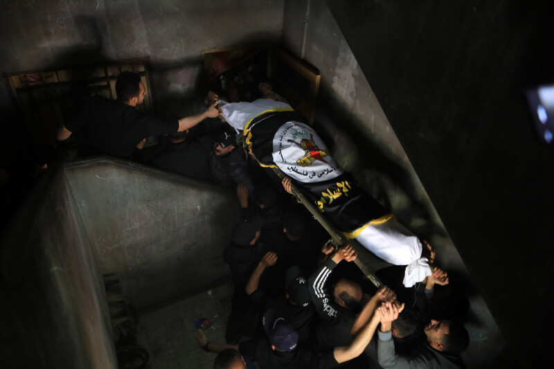 People carry a corpse wrapped in a flag down a staircase 