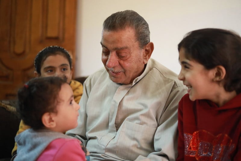 An elderly man smiles with three young children.